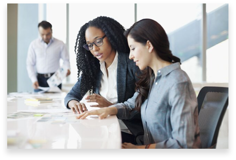 Two women are sitting at a table and one is looking at the other.