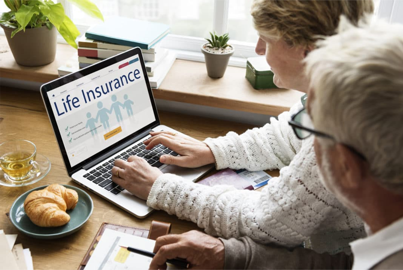 Two people are using a laptop to check life insurance.