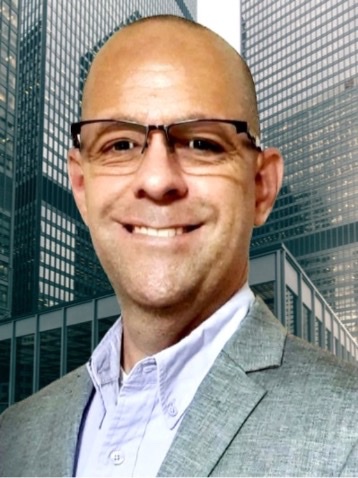 A man with glasses and bald head in front of some buildings.